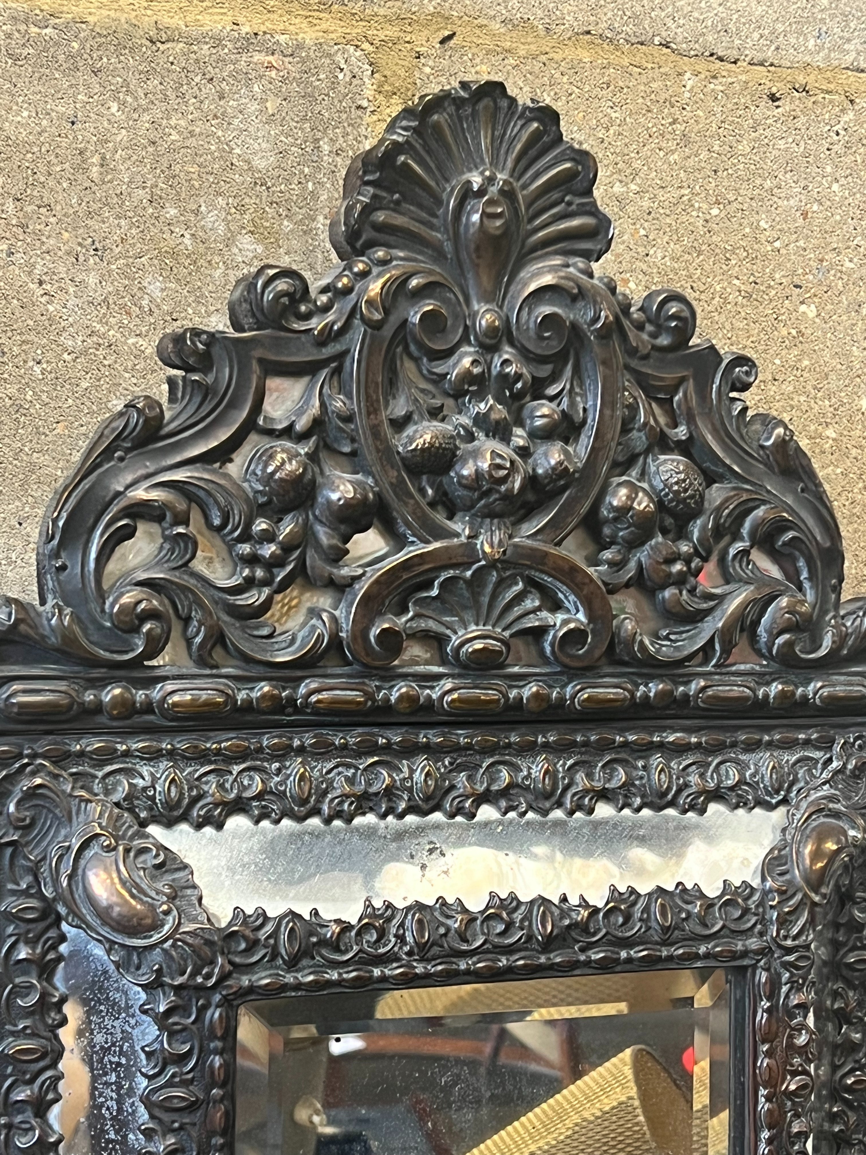 A Dutch brass framed cushion wall mirror, with ornate arched cresting, pierced and repousse with birds, scrollwork and shell surmount, width 33cm height 58cm